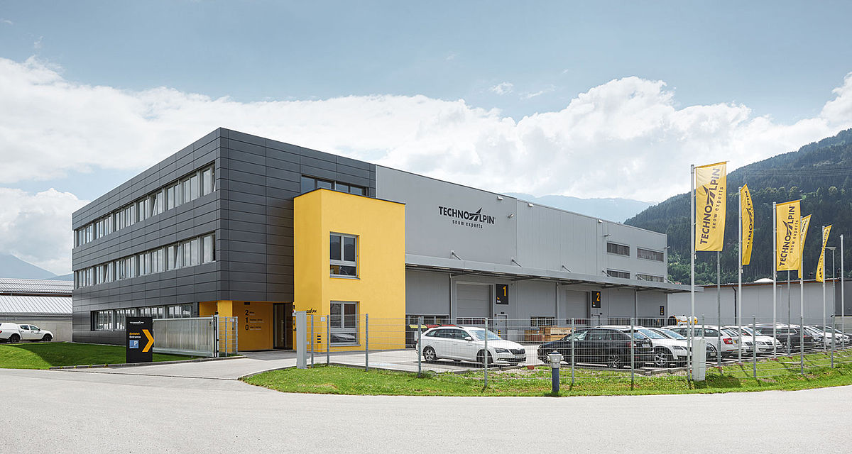 TechnoAlpin Standort Österreich mit Firmenflaggen und Alpenpanorama im Hintergrund