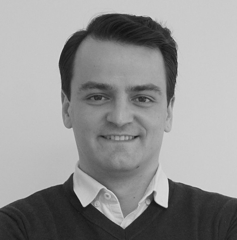 Florian Hajzeri, TechnoAlpin Mitarbeiter, Schwarz-Weiß-Portrait mit strahlendem Lächeln, gepflegtem dunklem Haar und dunklem Pullover