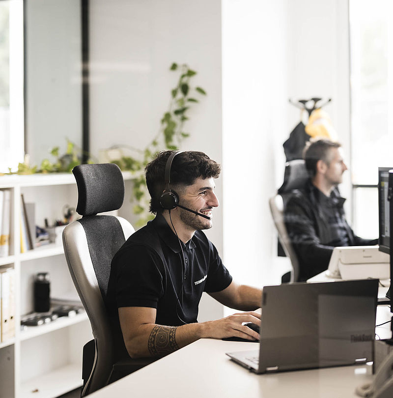 Smiling TechnoAlpin employee with headset at desk in bright office