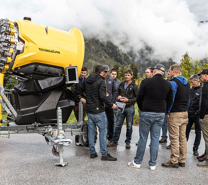 Gruppo visitatori davanti a innevatore a elica giallo TechnoAlpin durante presentazione del prodotto