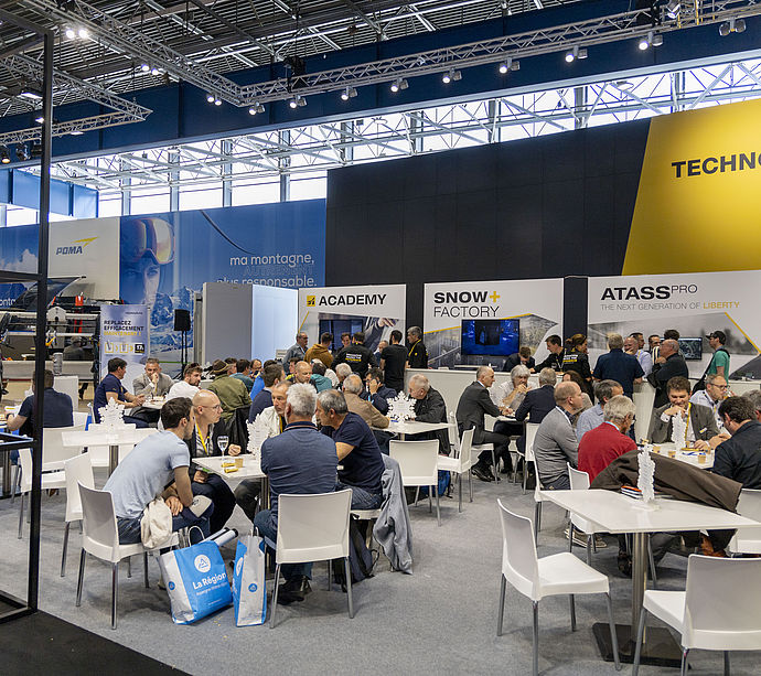 Overview of busy TechnoAlpin trade show stand with ATASS Pro, Academy and Snow Factory areas.
