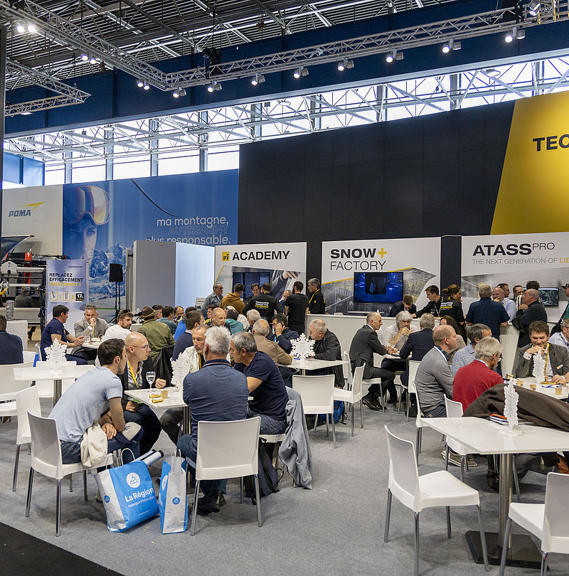 Overview of busy TechnoAlpin trade show stand with ATASS Pro, Academy and Snow Factory areas.