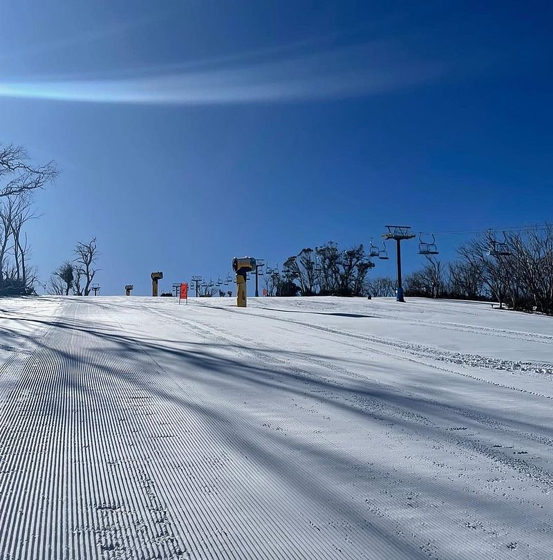 Frisch präparierte Skipiste mit Sesselliften und Schneeerzeugern unter strahlend blauem Himmel
