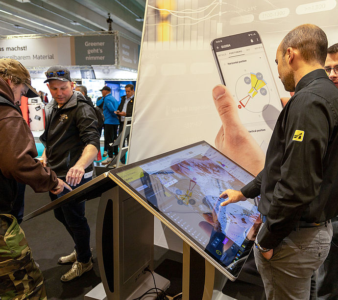 Interaktiver Touchscreen-Kiosk am TechnoAlpin Interalpin-Stand mit Beschneiungsapp, Karte und Positionierungsdaten, Mitarbeiter demonstriert