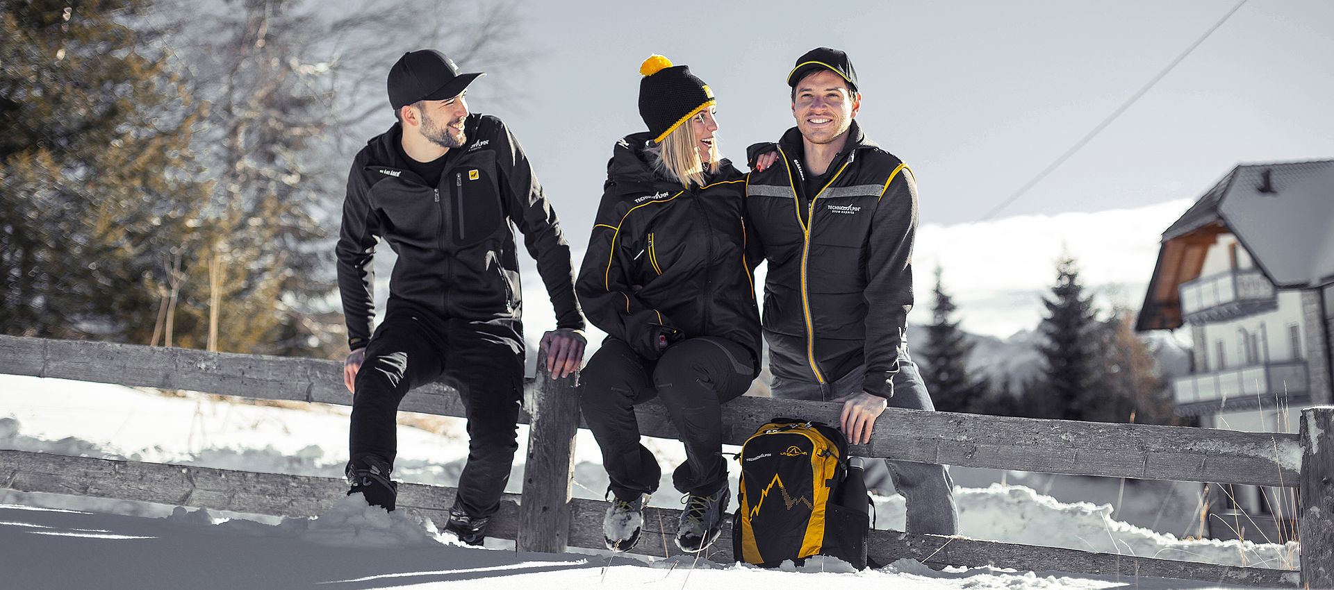 Drei TechnoAlpin Mitarbeiter in Arbeitskleidung lachen gemeinsam in winterlicher Berglandschaft