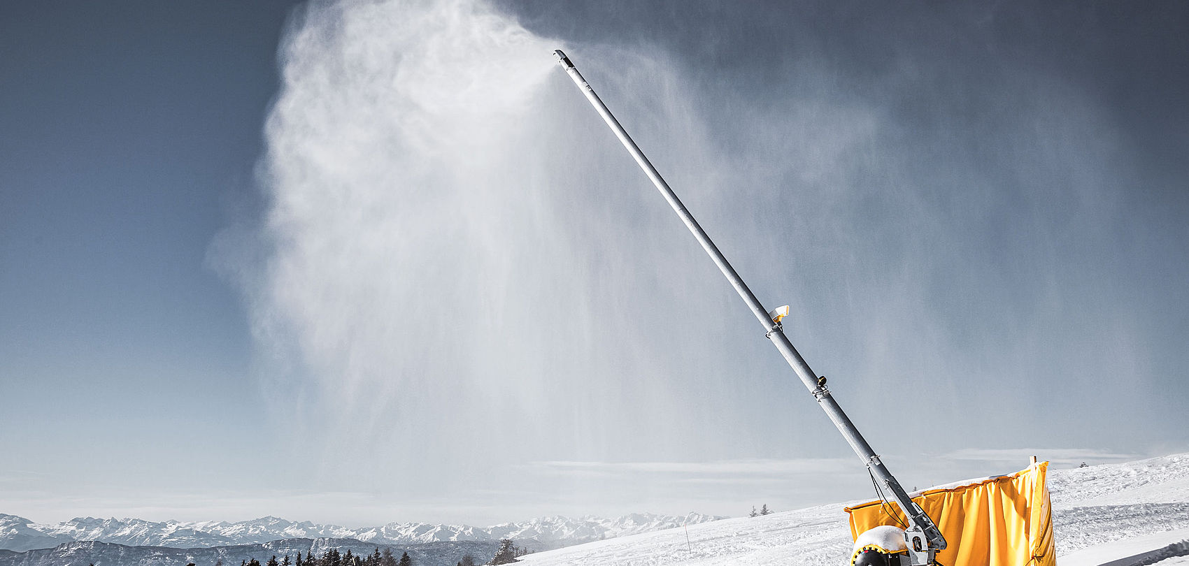Lancia da neve TechnoAlpin in funzione sulla pista da sci con panorama alpino