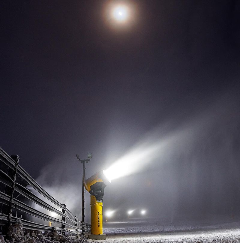 Gelbe TechnoAlpin Schneilanze leuchtet bei Nacht mit Vollmond am Himmel auf Skipiste
