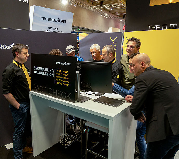 Besucher am TechnoAlpin Fact Check-Stand auf der Interalpin mit Dell-Monitor, der Beschneiungsberechnungen und Energieverbrauch zeigt