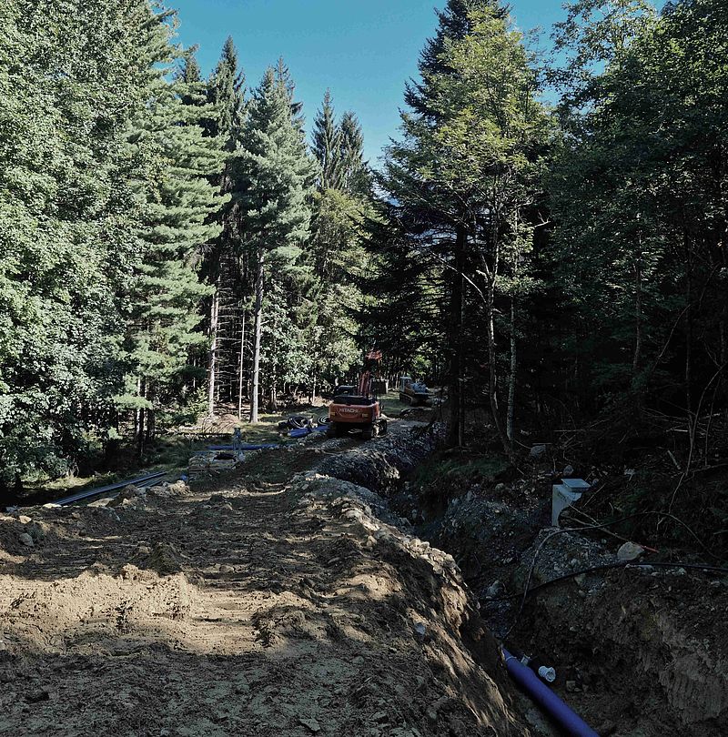 Baustelle im Wald mit Bagger und Verlegung von Rohrleitungen für Beschneiungsinfrastruktur