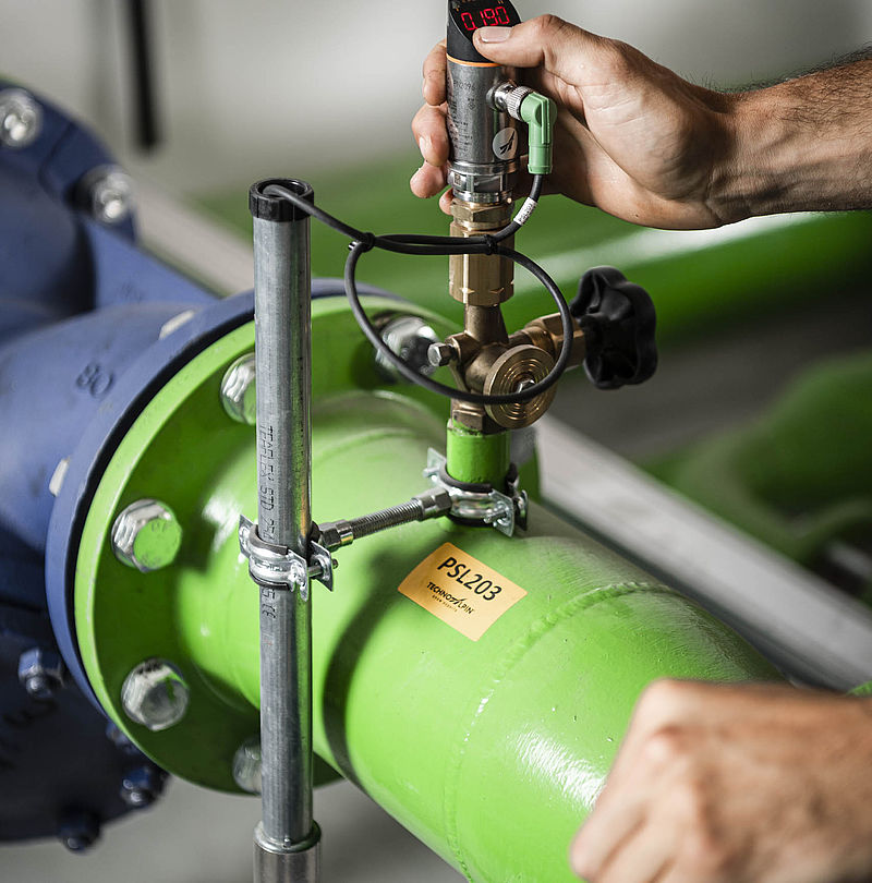 Nahaufnahme einer Hand bei der Montage eines Drucksensors an grüner Beschneiungsrohrleitung