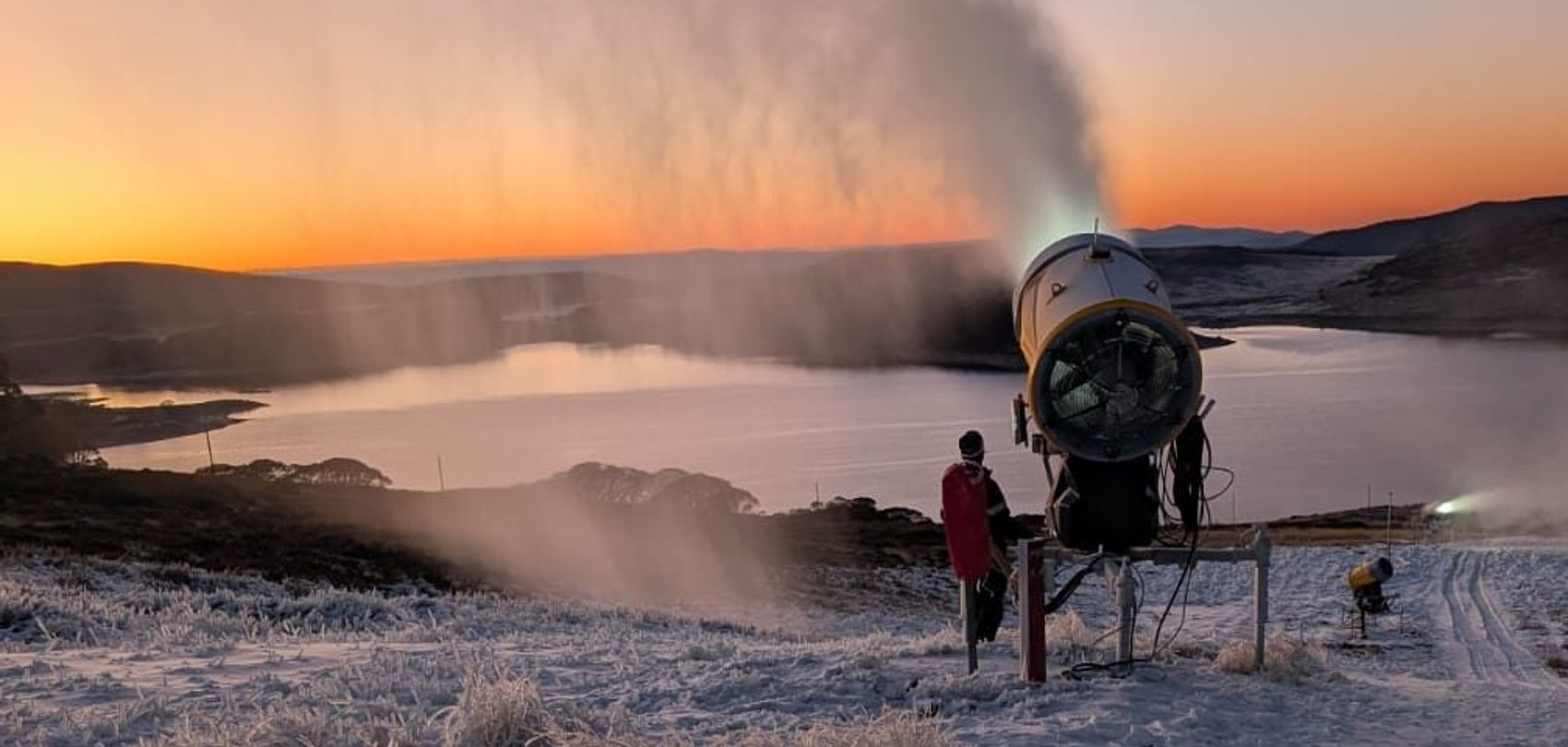 Schneekanone erzeugt Schnee bei Sonnenaufgang über See im Skigebiet Falls Creek