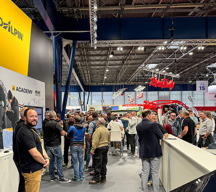 Überblick TechnoAlpin Messestand mit Academy-Bereich, Besuchern und Pistenbully im Hintergrund