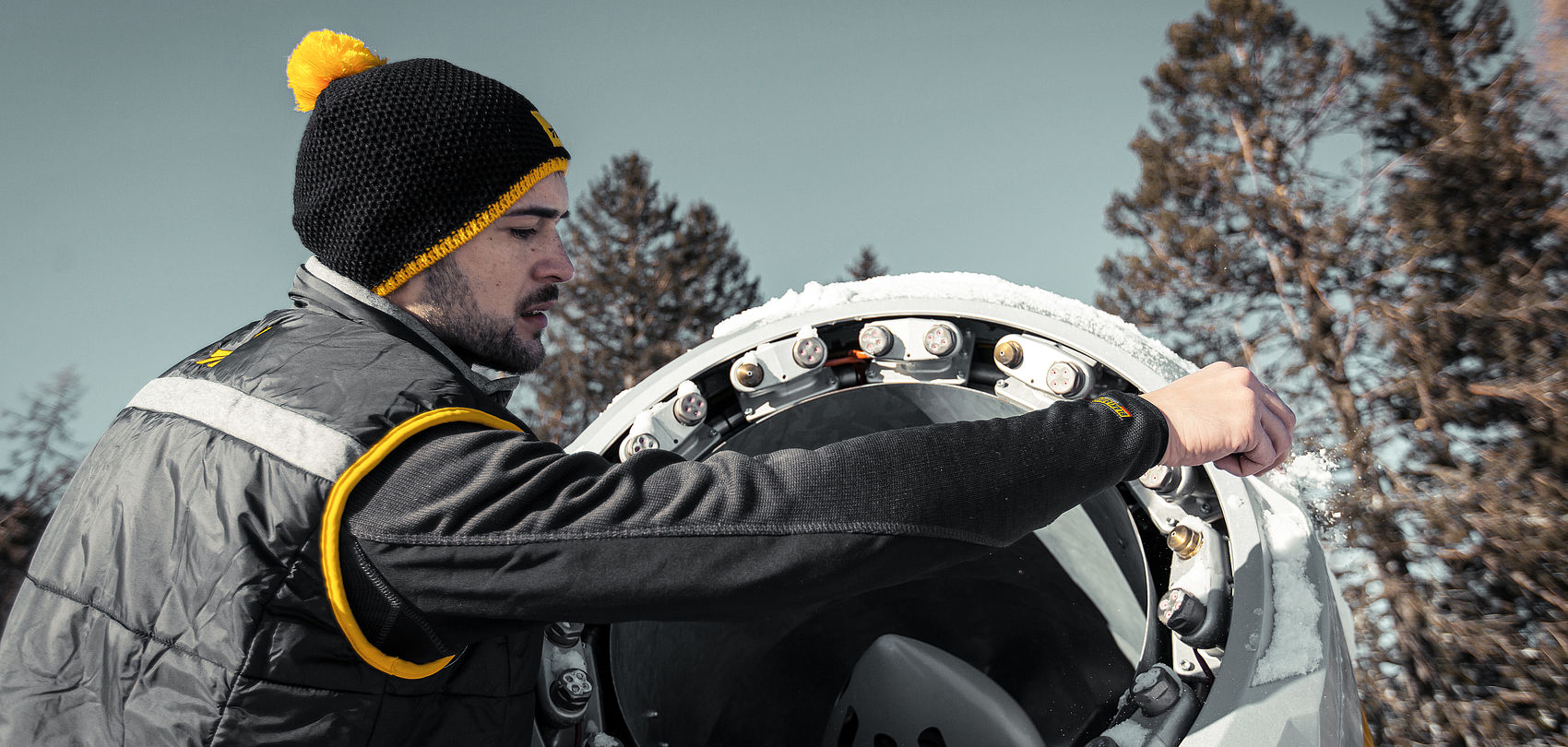 Technician with beanie inspecting nozzle ring opening of a snow gun in winter