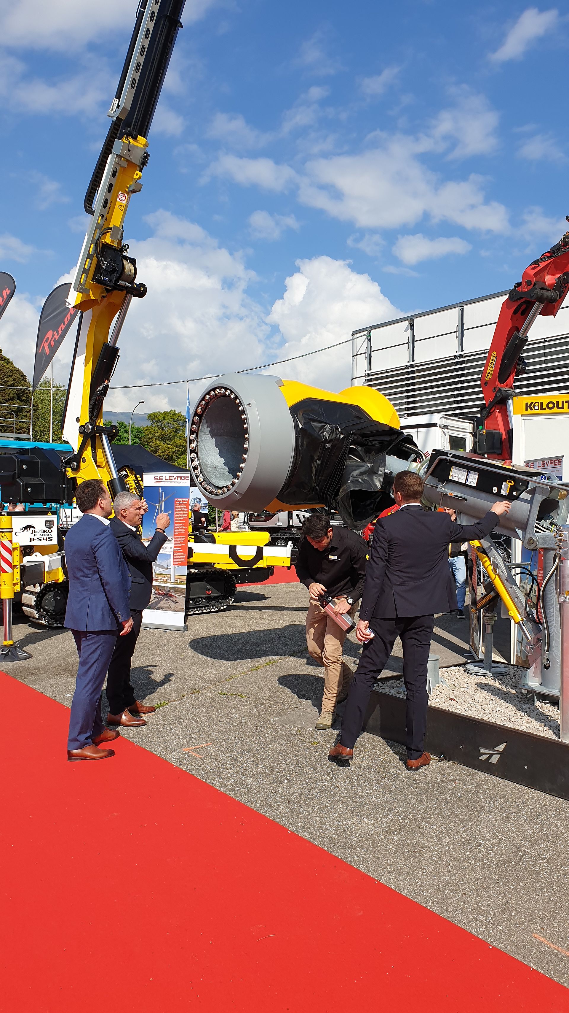 Outdoor presentation of TechnoAlpin snow gun with crane next to other machines under blue sky.