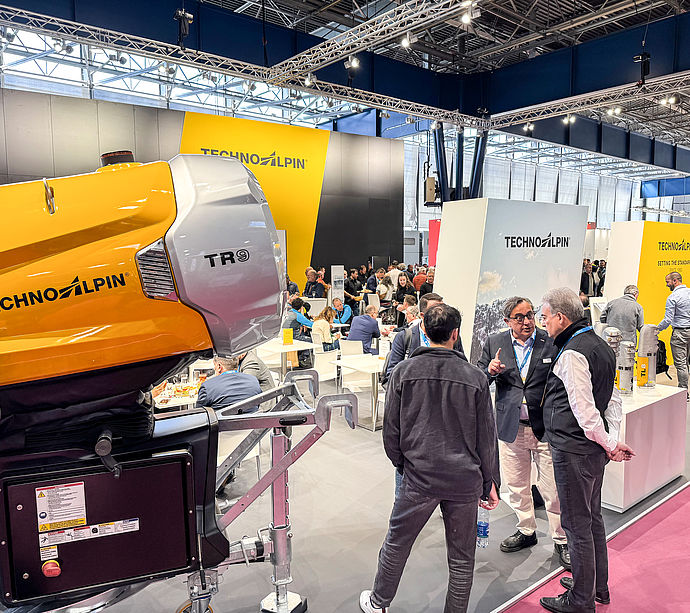 Gelber TR9 Propellerschneeerzeuger im Vordergrund, Berater im Gespräch am Messestand