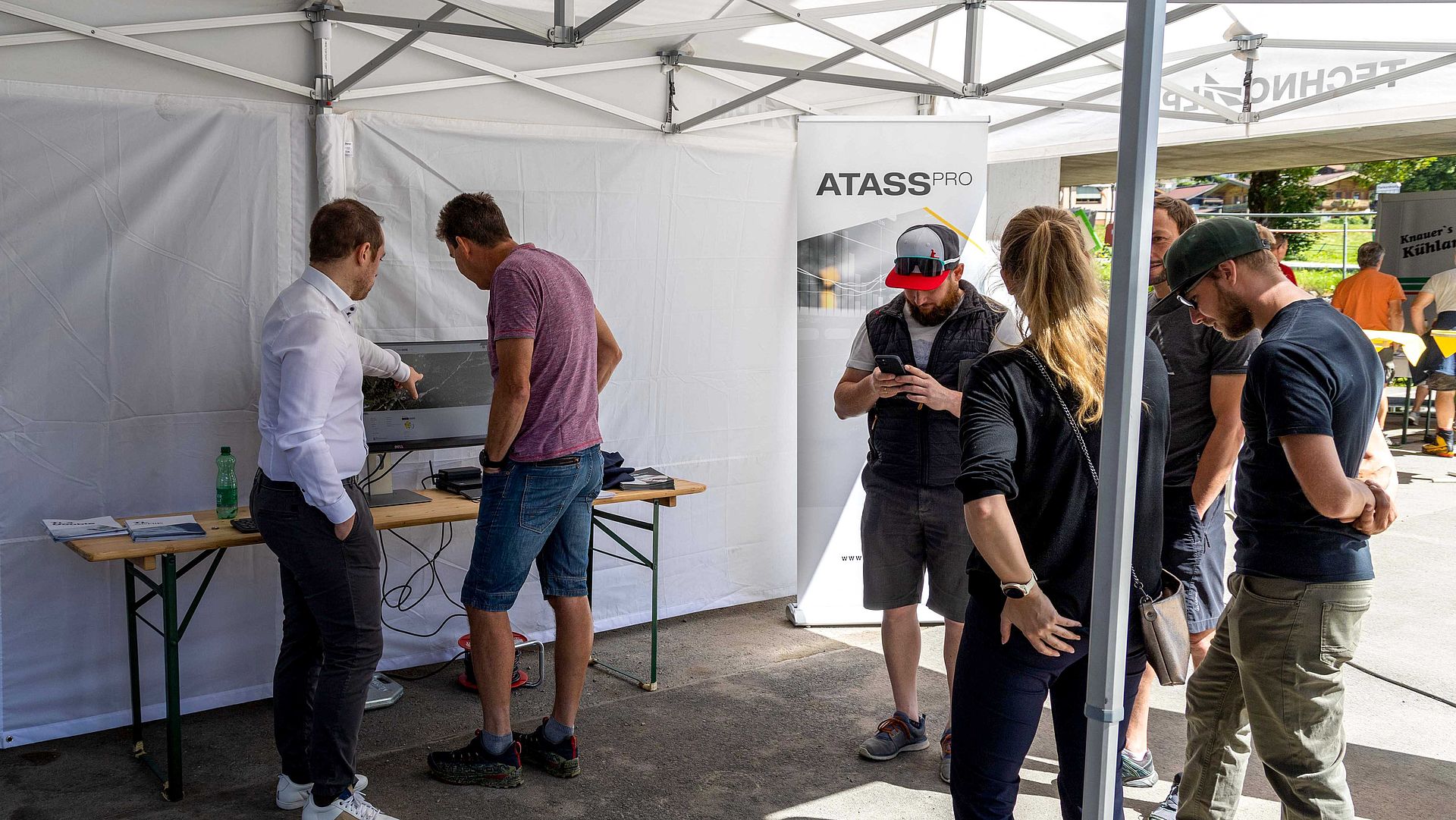 Visitors learning about ATASS Pro at info stand in tent at TechnoAlpin roadshow.