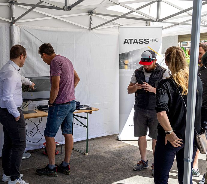 Visitors learning about ATASS Pro at info stand in tent at TechnoAlpin roadshow.