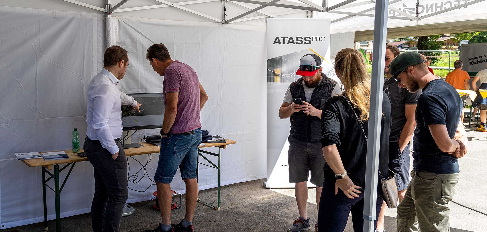 Visitors learning about ATASS Pro at info stand in tent at TechnoAlpin roadshow.