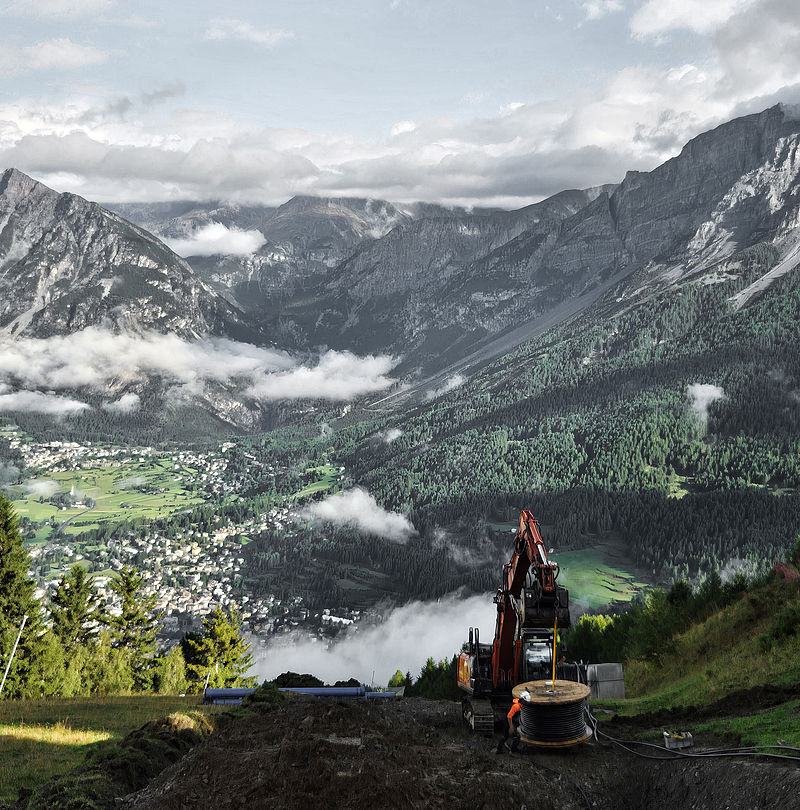 Escavatore con bobina cavi su cantiere sul fianco della montagna con vista panoramica