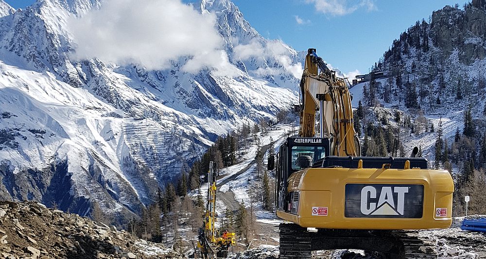 Escavatore Caterpillar sul cantiere impianto neve a Courmayeur con massiccio del Monte Bianco sullo sfondo