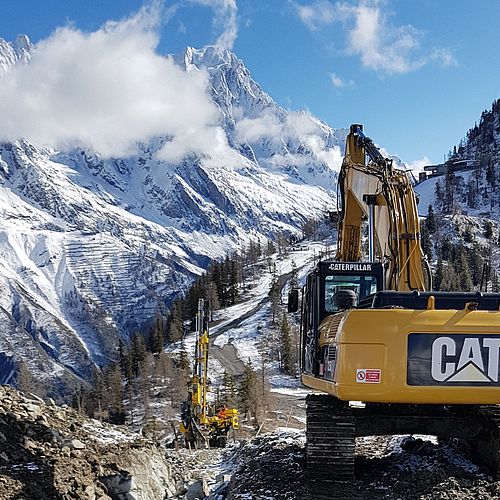 Caterpillar Bagger auf Beschneiungsbau-Baustelle in Courmayeur mit Mont Blanc Massiv im Hintergrund