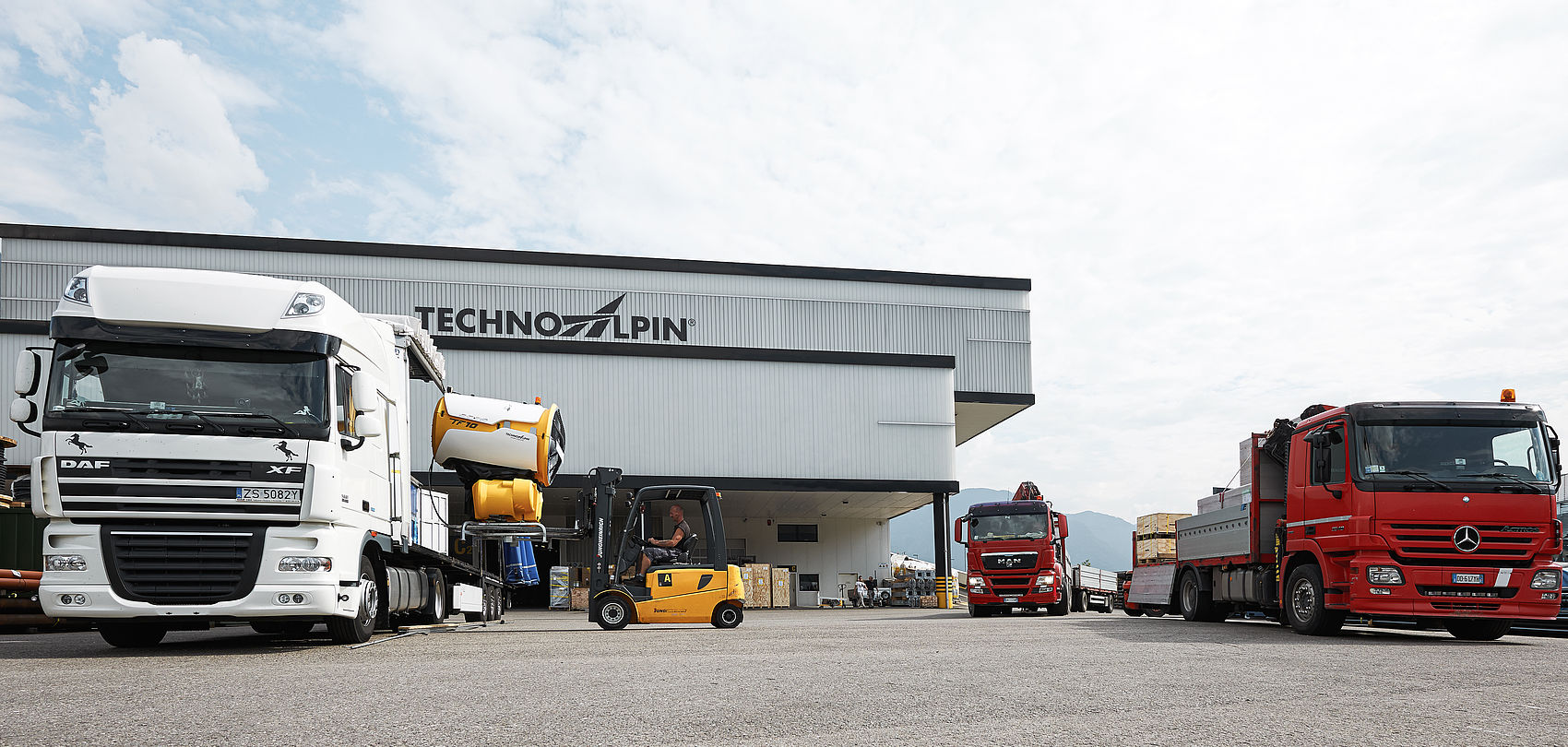 LKWs und Gabelstapler beim Verladen einer Schneekanone vor TechnoAlpin Versandhalle und Logistikzentrum