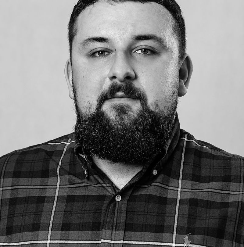 Andrej Križan, TechnoAlpin Mitarbeiter, Schwarz-Weiß-Portrait mit kurzem dunklem Haar, vollem Bart und neutralem Ausdruck in kariertem Hemd