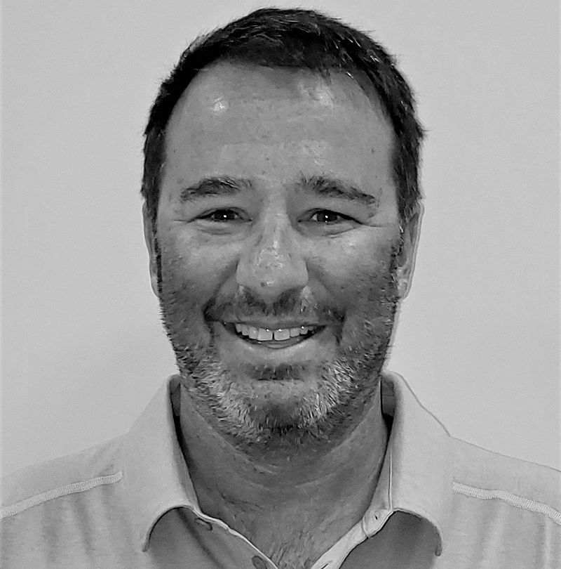 Todd Rudis, TechnoAlpin Mitarbeiter, Schwarz-Weiß-Portrait mit freundlichem Lächeln, kurzem dunklem Haar und Dreitagebart im Polo-Shirt