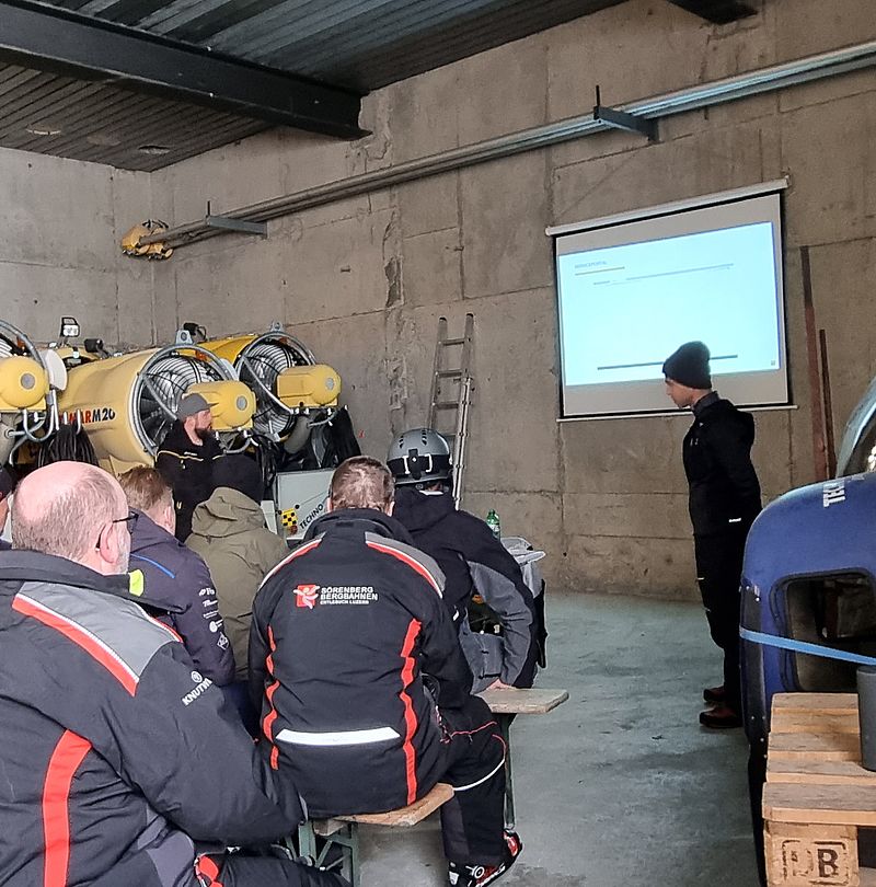Formazione TechnoAlpin in officina con partecipanti davanti a schermo accanto a generatori di neve gialli.