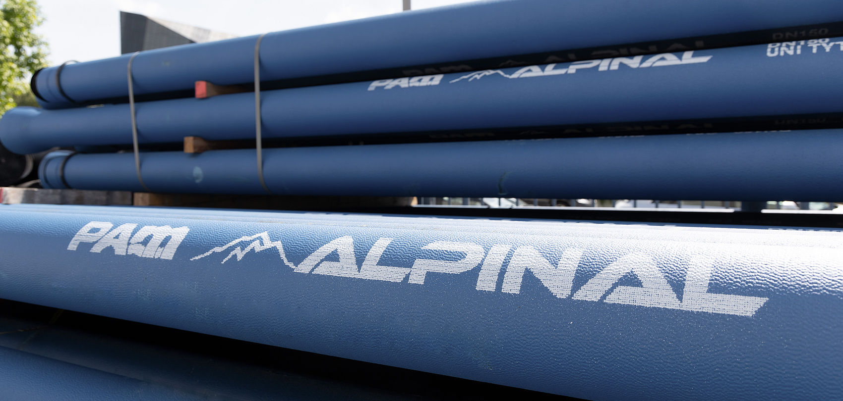 Stack of blue Alpinal pipes with white PAM logo outdoors.